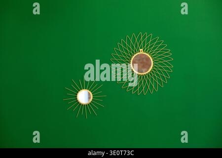 Intérieur minimaliste avec des miroirs de soleil dorés décoratifs sur un mur vert. Concept de décoration murale moderne avec espace de copie, pièce intérieure élégante Banque D'Images