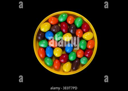 Bonbons au chocolat multicolores dans un bol jaune sur fond noir Banque D'Images