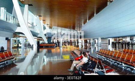 Doha, Qatar - 12 avril 2019 : jeunes couples inconnus de touristes assis sur un banc et attendant leur vol à l'aéroport international moderne Banque D'Images