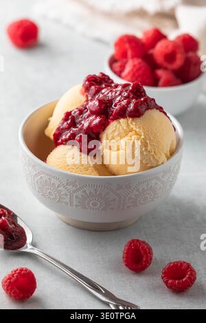 Un bol de sorbet à la mangue garni de coulis de framboises avec des framboises fraîches. Banque D'Images