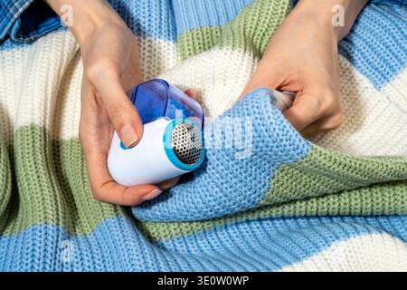 Rasoir en tissu dans les mains enlevant les peluches et boulochage du pull tricoté. Concept de soin durable des vêtements prolongeant la durée de vie des vêtements, maintenant le tricot Banque D'Images