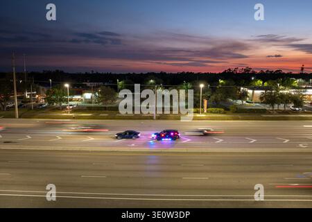La circulation nocturne s'arrête sur la rue USA City pendant que la police s'arrête sur le véhicule qui accélère. Les feux des voitures de patrouille clignotent dans un environnement de circulation urbaine. Banque D'Images