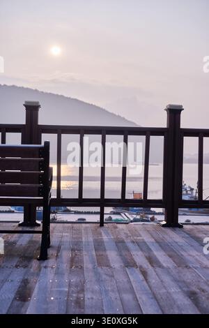 Coucher de soleil mélancolique au port de Mangdeok avec une terrasse en bois tranquille, un banc vide et un café vintage rose délavé, évoquant la nostalgie et la solitude. Banque D'Images