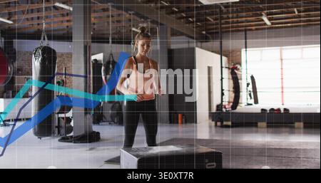 Femme debout dans des leggings de réservoir de pêche faisant box-jump derrière plyo box boxe gym, avec des sacs de punching Banque D'Images