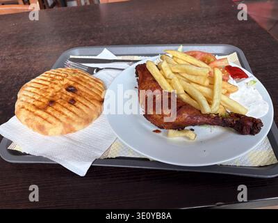 Restauration rapide italienne abordable avec cuisse de poulet grillée, frites, salade fraîche et pain plat grillé, déjeuner à petit budget typique. Banque D'Images