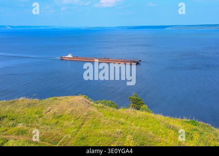 Un remorqueur articulé et un vraquier à barge transportent du sable et des matériaux de construction sur la rivière. La grande barge navigue le long de la large rive de la Volga Banque D'Images