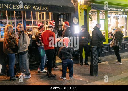 Londres, Royaume-Uni, 2 décembre 2025, Groupe de personnes portant des chapeaux de Père Noël buvant devant le pub Princess of Wales la nuit à Londres. Banque D'Images