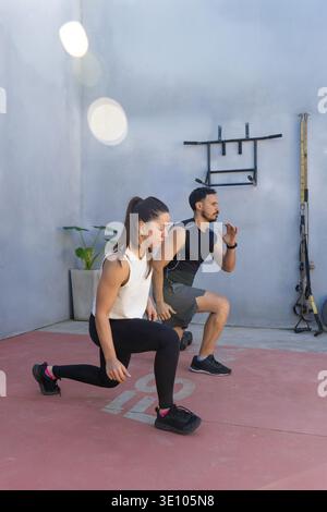 Deux professionnels du fitness démontrant une forme de fente appropriée dans une zone d'entraînement en plein air, soulignant la force, la flexibilité et l'équilibre tout en favorisant Banque D'Images