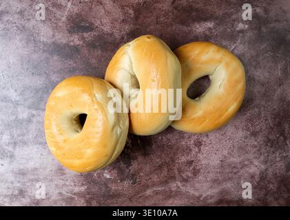 Vue de dessus de trois bagels Unis sur un plateau de table rouge marbré illuminé d'un éclairage naturel. Banque D'Images