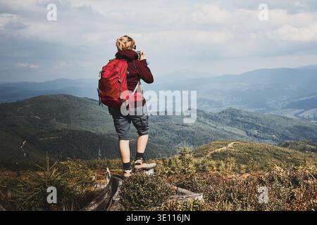 Femme avec sac à dos de randonnée dans les montagnes. Passer des vacances d'été près de la nature. Vue arrière d'une femme debout sur une souche en haut de la colline en admirant la mounta Banque D'Images