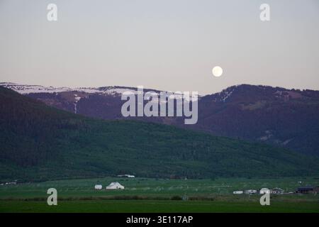 La pleine lune commence à apparaître au crépuscule avec des montagnes couvertes de neige en vue. Idaho USA Banque D'Images