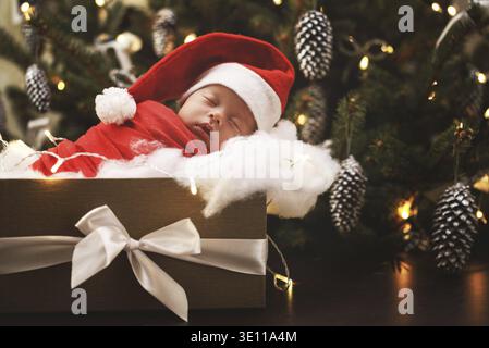 Bébé nouveau-né mignon portant chapeau de Père Noël dort dans la boîte cadeau de Noël. Joyeux Noël et bonne année Banque D'Images