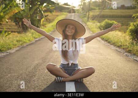 La jeune femme heureuse est assise au milieu de la route asphaltée Banque D'Images