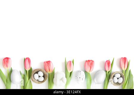 Fond blanc de Pâques avec tulipes roses, œufs dans les nids et un lapin. Espace de copie, vue de dessus, pose à plat. Banque D'Images