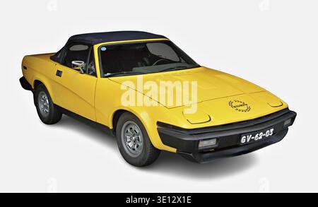 Cabriolet Triumph TR7 jaune classique garé sur un fond blanc, arborant son logo Triumph Banque D'Images