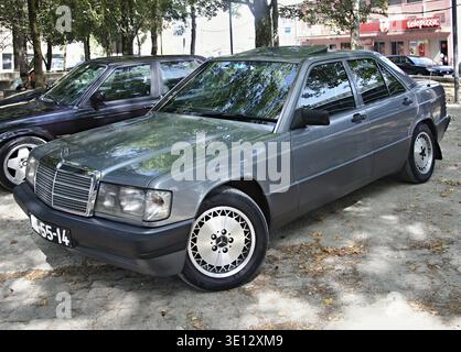 Mercedes-Benz 190E grise garée à l'ombre de quelques arbres près d'un restaurant Telepizza Banque D'Images