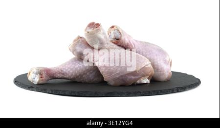 Quatre pilons de poulet cru reposant sur une planche à découper en ardoise noire. En attente d'assaisonnement et de cuisson. Placez-le sur un fond blanc propre. Mettre en surbrillance fr Banque D'Images