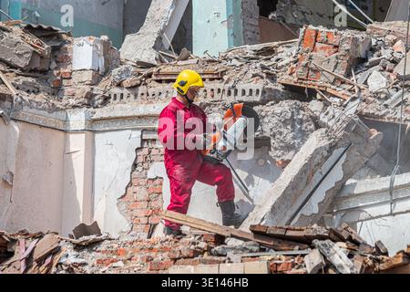 Le sauveteur en équipement de protection utilise une scie électrique pour couper les structures en béton et en métal lors de l'enlèvement des débris sur un chantier endommagé Banque D'Images