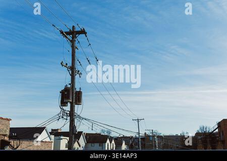 Les poteaux électriques se dressent au-dessus des maisons dans une zone suburbaine. Des fils relient les poteaux aux maisons ci-dessous sous un ciel bleu clair. La scène montre Daily Lif Banque D'Images