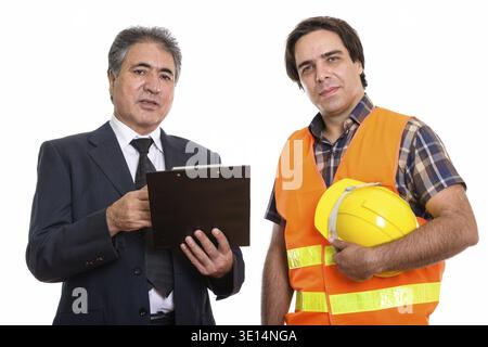Studio shot of Persian senior businessman holding clipboard avec jeune homme persan construction worker Banque D'Images