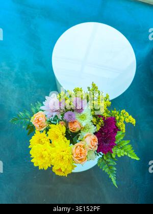 Un vase tient des fleurs lumineuses avec différentes couleurs sur une table ronde. La table repose sur une surface bleue et la lumière du jour brille sur la scène. Banque D'Images