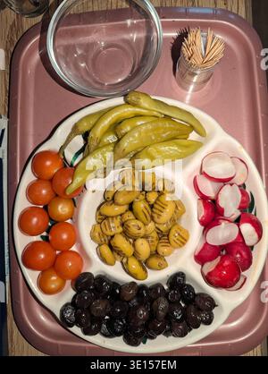 Plateau avec olives radis tomates pistaches. Vibrant Meze étalé sur plateau en céramique, verre d'eau et pot de cure-dents, couleurs vives et contrastées Banque D'Images