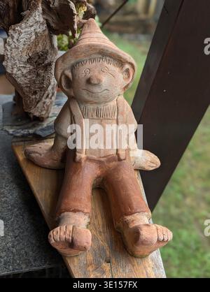 Figurine de Gnome de jardin d'argile sur Ledge, expression accueillante avec chapeau incliné, texture en terre cuite altérée et détails peints, planche en bois rustique et B. Banque D'Images