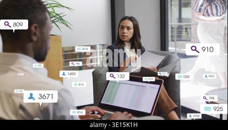 Femme assise portant blazer marine tenant des papiers dans le bureau, ordinateur portable montrant des données et des icônes de superposition Banque D'Images