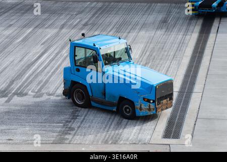 Véhicule de remorquage d'aéroport manœuvrant sur le tarmac à proximité de l'infrastructure de service, mettant en évidence les systèmes de manutention au sol, le mouvement côté piste et l'aviati moderne Banque D'Images
