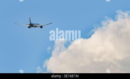 Avion commercial volant dans un ciel bleu clair avec des nuages blancs moelleux, vue arrière Banque D'Images