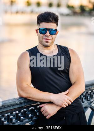 Jeune homme au physique athlétique portant des lunettes de soleil bleues à l'extérieur Banque D'Images