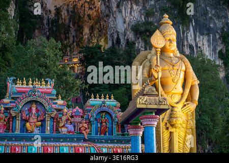 Grottes de Batu, Malaisie – 3 février 2020 : une statue dorée du Seigneur Murugan se dresse à côté des sanctuaires colorés du temple hindou sur les falaises de calcaire des grottes de Batu. Banque D'Images