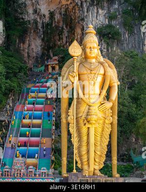 Grottes de Batu, Selangor/Malaisie – 3 février 2020 : une grande statue dorée se dresse à côté de l’escalier coloré menant à l’entrée de la grotte. Banque D'Images