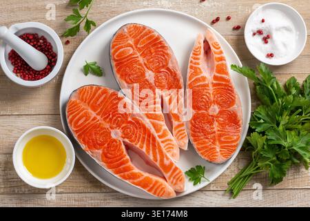 steaks de saumon crus sur plaque blanche, fond en bois, vue de dessus Banque D'Images