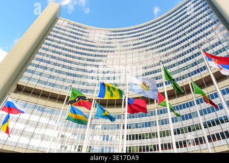 Vienne, Autriche - 25 février 2026 : des drapeaux nationaux colorés branlent fièrement sur des poteaux contre la façade en verre incurvée de l'emblématique Vienna International Banque D'Images