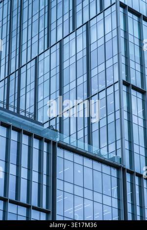 La façade en verre bleu frappante d'un immeuble de bureaux moderne met en valeur une architecture d'entreprise élégante. Les surfaces réfléchissantes et les lignes géométriques ajoutent un conte Banque D'Images