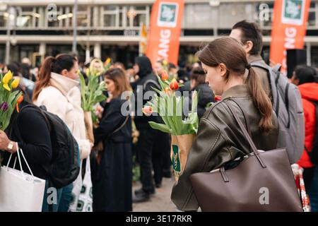 Berlin, Allemagne - 14 mars 2026 : les visiteurs portant des bouquets de tulipes colorés se réunissent lors d'un festival de fleurs public en plein air à Berlin, avec des drapeaux d'événement an Banque D'Images