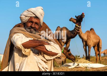 Portrait d'un homme assis dans un turban avec des chameaux pâturant au loin à la foire des chameaux de Pushkar à Pushkar pendant les heures du matin. Banque D'Images