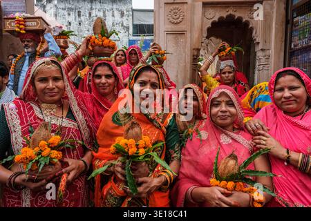 Les femmes de Pushkar portant des saris vibrants sourient à la caméra tout en tenant des pots cérémoniels en argile ornés de soucis oranges et de feuilles vertes. Banque D'Images