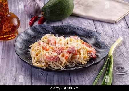 Une délicieuse assiette de spaghettis crémeux avec des morceaux de saumon et du parmesan. Le plat est présenté sur un fond en bois gris rustique avec I frais Banque D'Images
