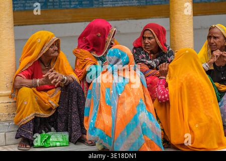 Un groupe de femmes portant des voiles traditionnels orange et rouge sont assis ensemble sur le sol à Pushkar, engagés dans la conversation près d'une colonne de temple. Banque D'Images