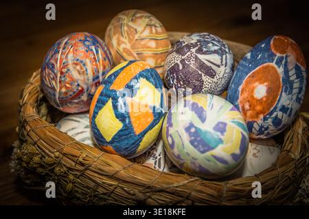 Un panier rustique tissé rempli d'œufs de Pâques colorés en soie aux motifs géométriques et floraux complexes. Banque D'Images