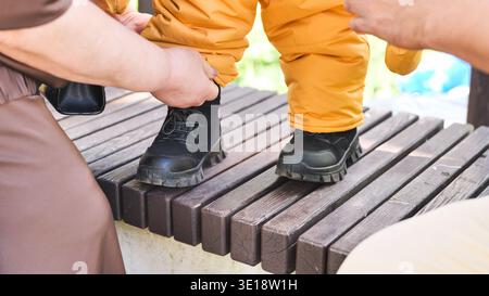 Mains adultes aidant l'enfant, apprenant à marcher dehors, gros plan sur les pieds Banque D'Images