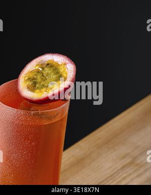 Un cocktail vibrant à la riche teinte orange est servi dans un grand verre, surmonté d'une tranche fraîche de fruits de la passion. La boisson repose sur un s en bois texturé Banque D'Images