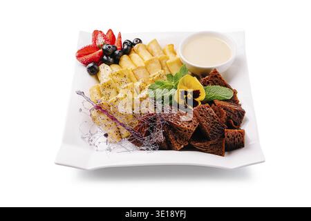 Le plateau de desserts coloré présente une gamme de fruits frais comme les fraises et les bananes, associés à des friandises décoratives. Une trempette crémeuse complemen Banque D'Images