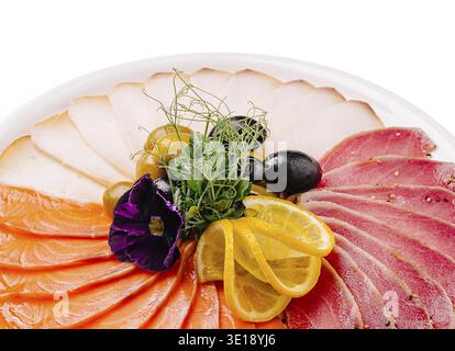 Un plat magnifiquement arrangé avec du saumon finement coupé en tranches, du thon en croûte de poivre et des tranches de viande blanche, garni de tranches de citron, noir et gree Banque D'Images