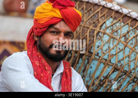 Portrait d'un homme barbu portant un turban rouge et jaune vif et une écharpe rouge assis à côté d'un grand tambour à Pushkar Mela. Pushkar Rajast Banque D'Images