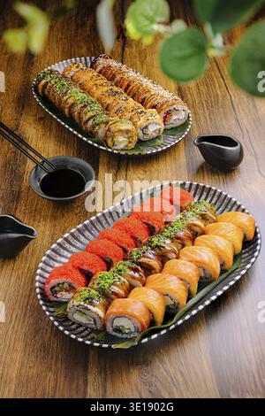 De délicieux rouleaux de sushi sont agencés avec art sur deux assiettes, présentant une variété de couleurs et de textures. Un plat de sauce soja et des baguettes sont placés Alo Banque D'Images