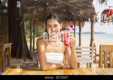 Jeune femme buvant une boisson de pastèque à la plage en Thaïlande Banque D'Images