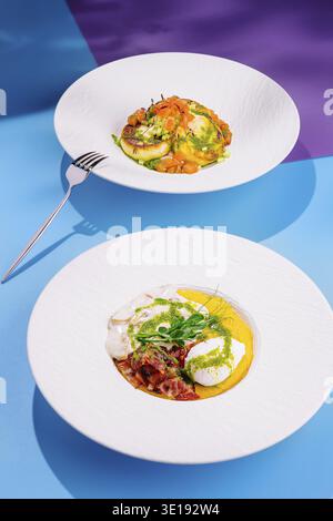 Deux plats exquis sont servis sur des assiettes blanches, mettant en valeur un arrangement vibrant de couleurs et de textures sur un fond bleu et violet vif Banque D'Images